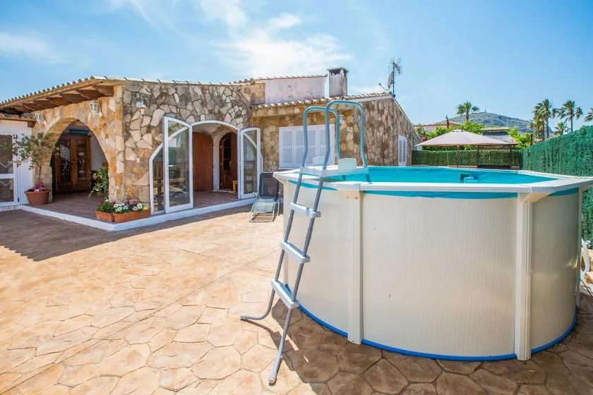 Un patio pavimentado con una piscina elevada junto a una casa de piedra.