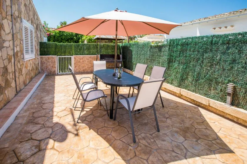 A paved outdoor patio with a dining table and seating beneath a large umbrella.