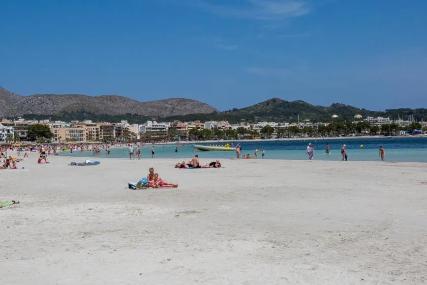 A broad sandy beach with people by the shoreline and hills in the distance.