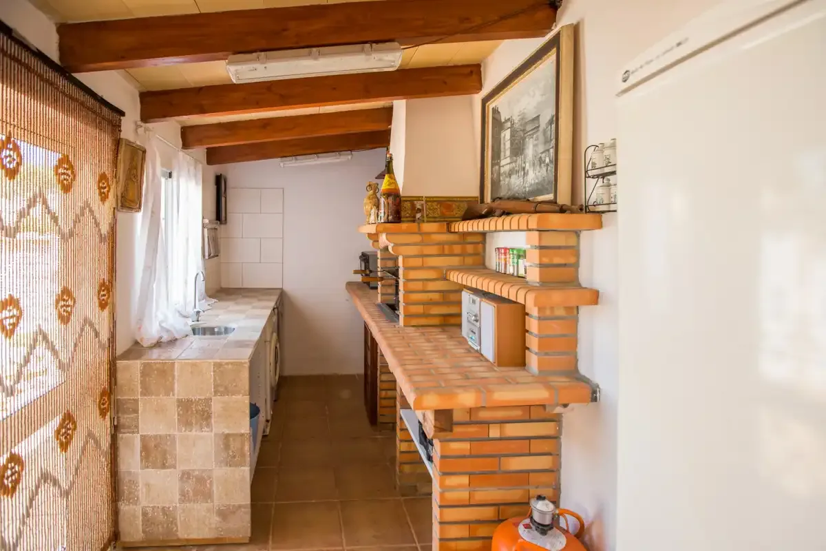 A narrow kitchen with a tiled counter, brick shelving, and exposed wooden ceiling beams.