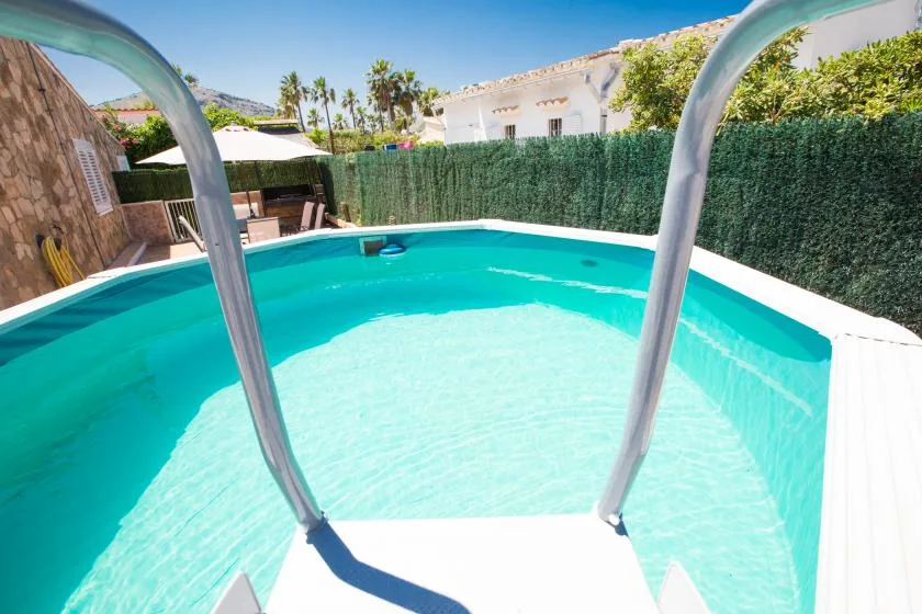 Una pequeña piscina al aire libre con agua turquesa junto a un seto.