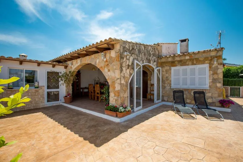 Una casa de piedra da a un patio soleado pavimentado con asientos al aire libre.