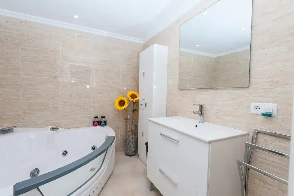 A tiled bathroom with a corner whirlpool tub and white vanity.