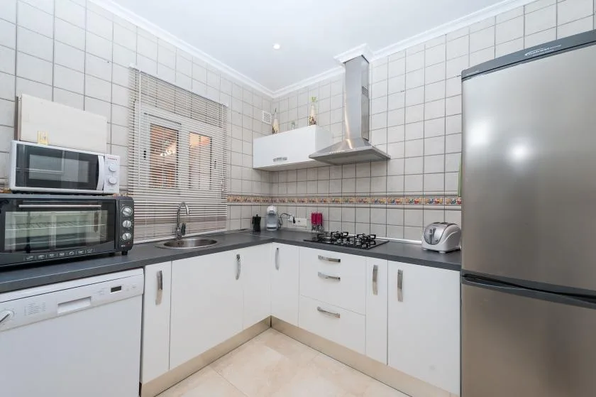 A tiled kitchen with white cabinets, a countertop, and stainless steel appliances.