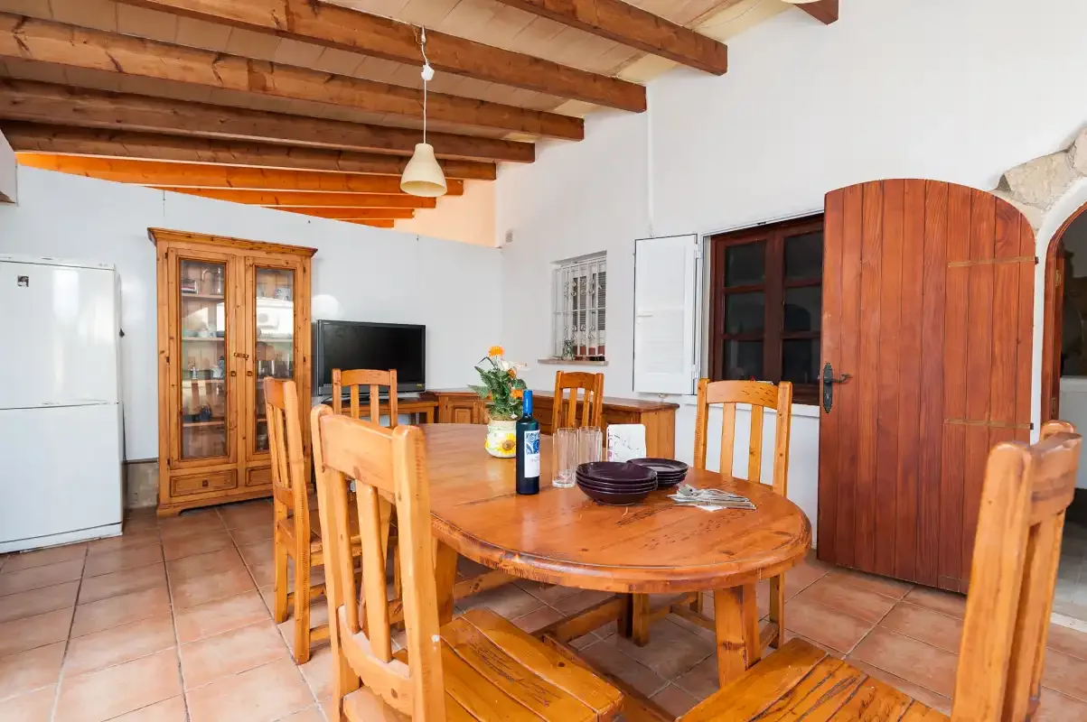 A dining room with a wooden table and chairs beneath exposed ceiling beams.