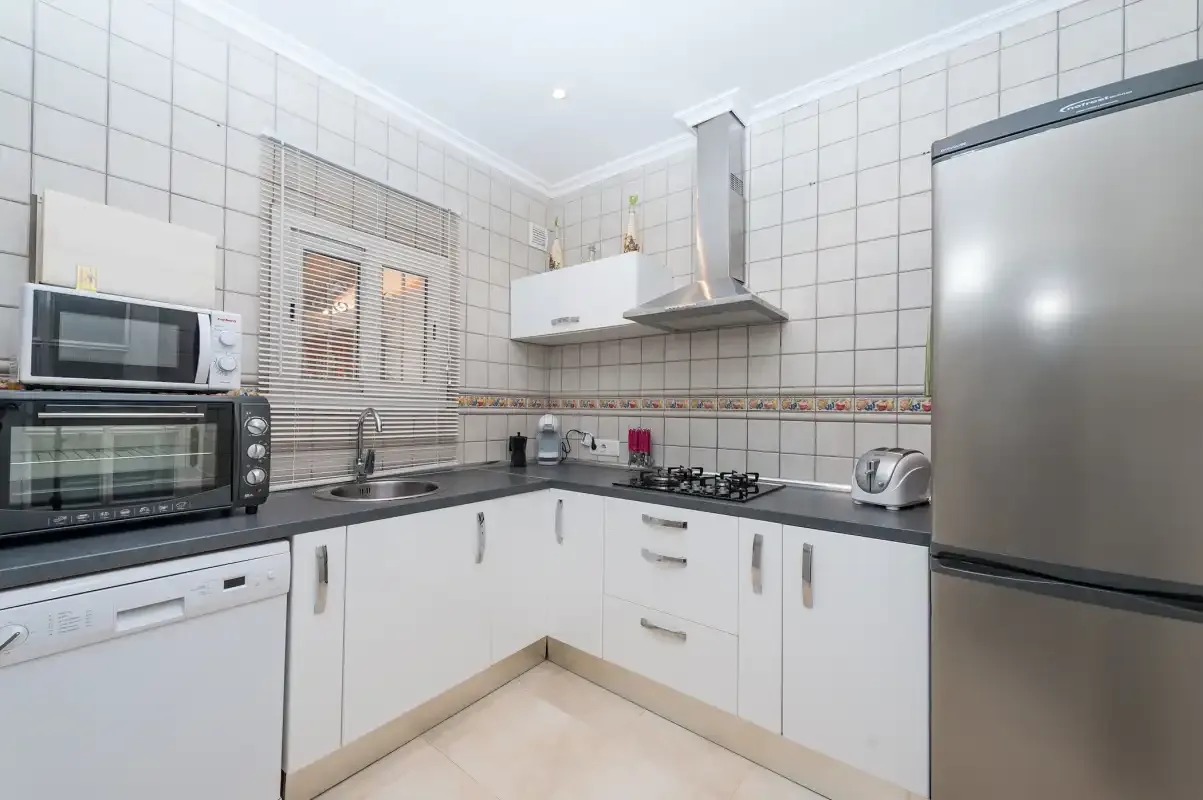 A tiled kitchen with white cabinets, appliances, and a countertop.