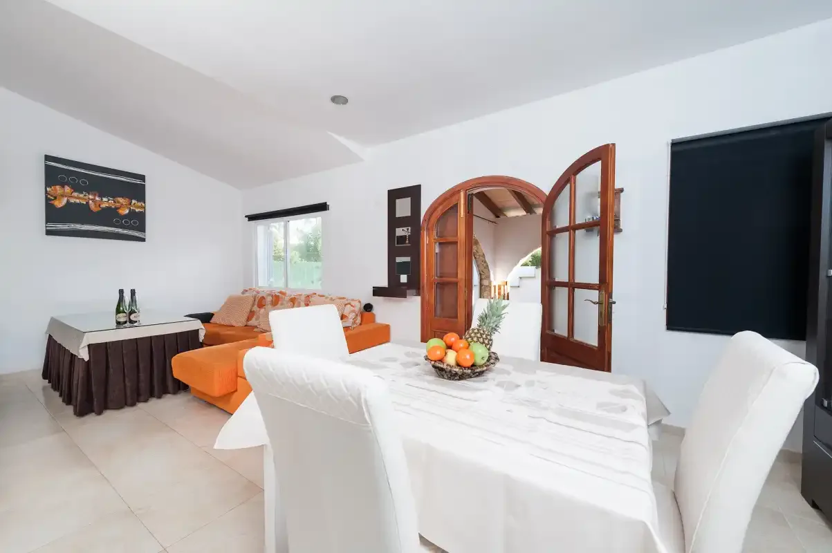 A bright dining and sitting area with a table, seating, and an open wooden doorway.