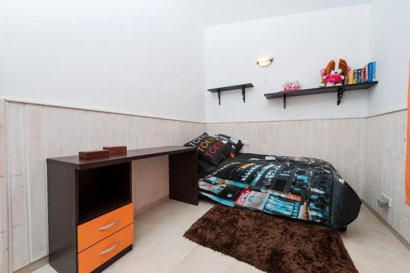 A bedroom with a desk, bed, and brown rug.