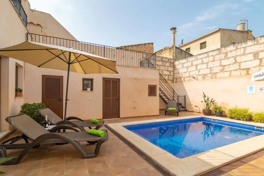 An outdoor pool beside a patio with lounge seating and a large umbrella.
