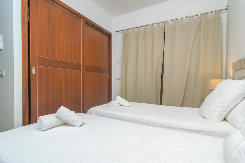 A bedroom with two beds, a wooden wardrobe, and beige curtains.