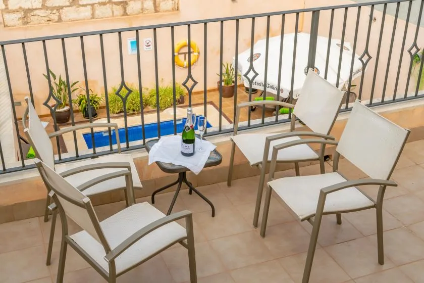 A small balcony seating area overlooks a pool, with a table and chairs.