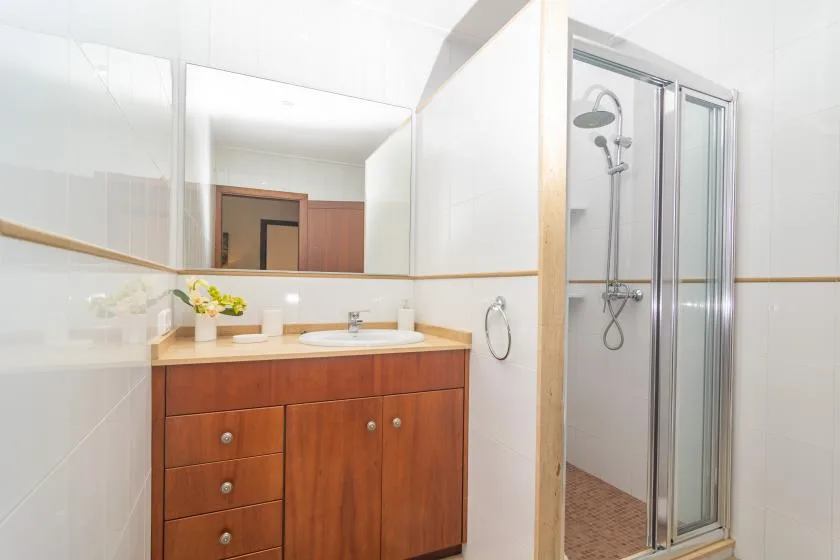 A bright tiled bathroom with a wooden vanity and a glass-enclosed shower.