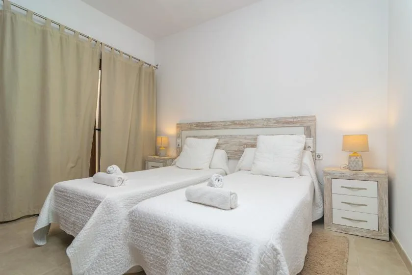 A bedroom with two beds, white bedding, and beige curtains.