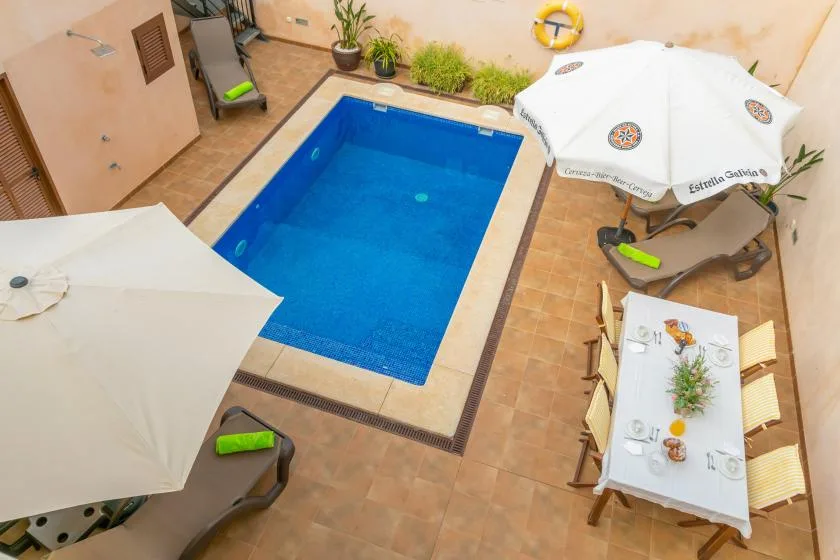 A small outdoor pool sits beside a table and shaded seating.