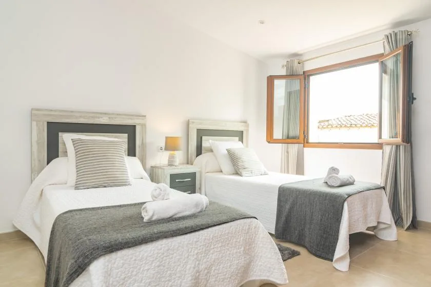 A bright bedroom with two beds and an open window.