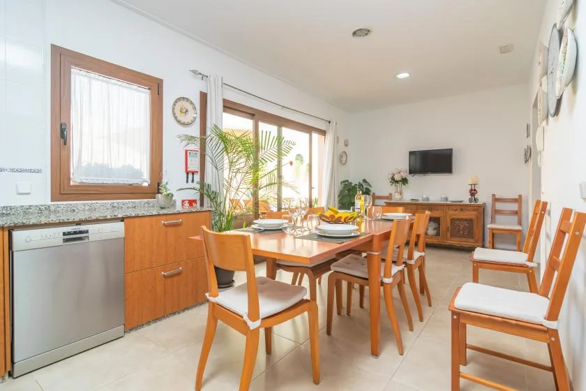 A dining area with a wooden table and chairs beside bright windows.