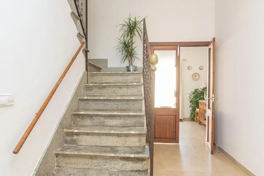 An indoor stairway with stone steps and a wooden handrail leads to a bright hallway.