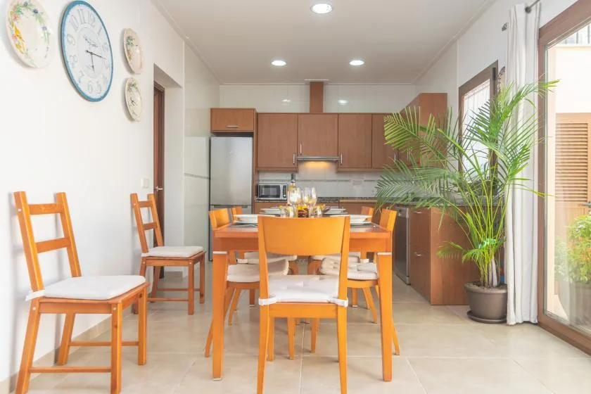 A dining area with wooden seating beside an open kitchen and potted plants.