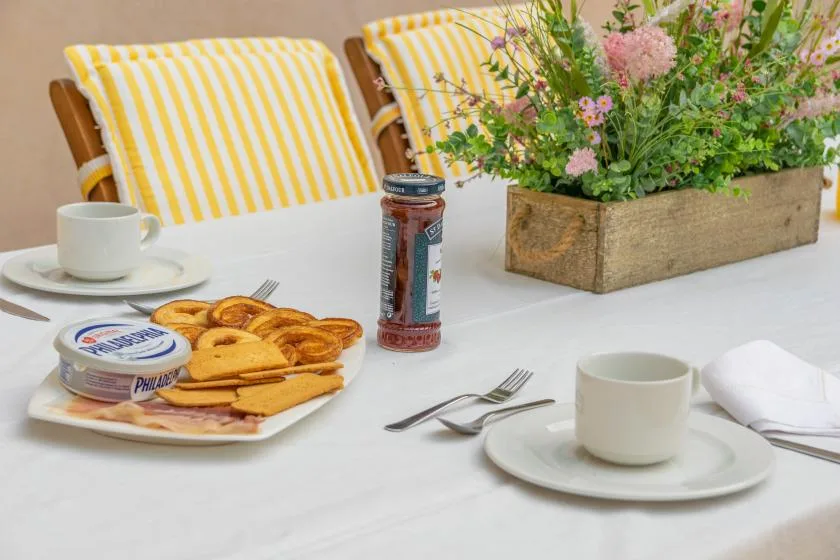 A breakfast table with pastries, coffee cups, and a flower arrangement.