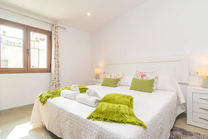 A bright bedroom with a white bed, green cushions, and a window.
