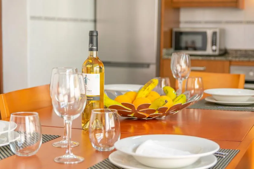 A dining table is set with wine glasses, a bottle, fruit, and a plate.