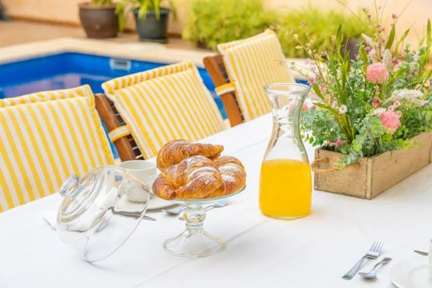 A breakfast table with pastries and juice sits beside a pool.