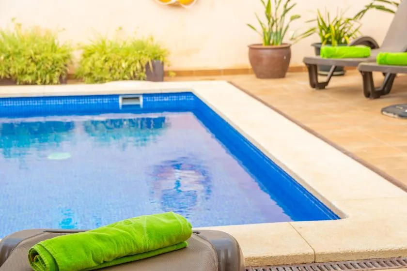 An outdoor swimming pool bordered by light-colored paving and lounge seating.