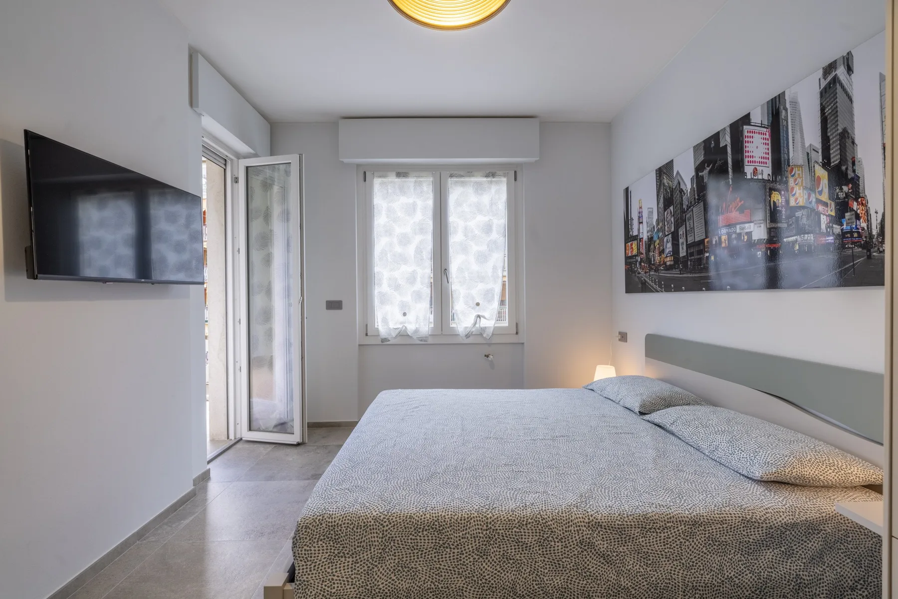 Un dormitorio con una cama grande, un televisor en la pared y una ventana con cortinas.