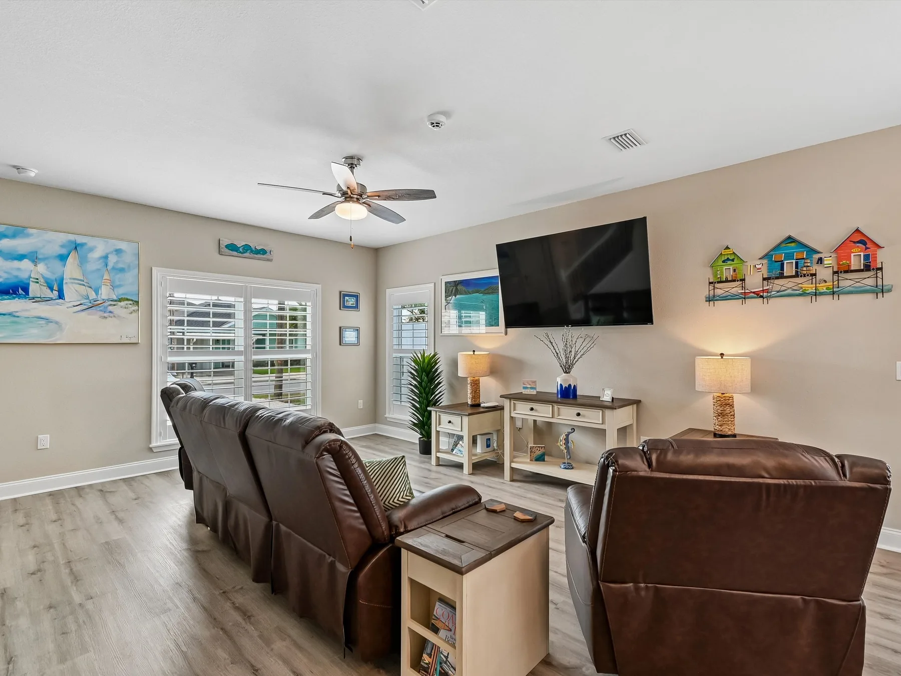 A living room with brown seating, a wall-mounted television, and a ceiling fan.