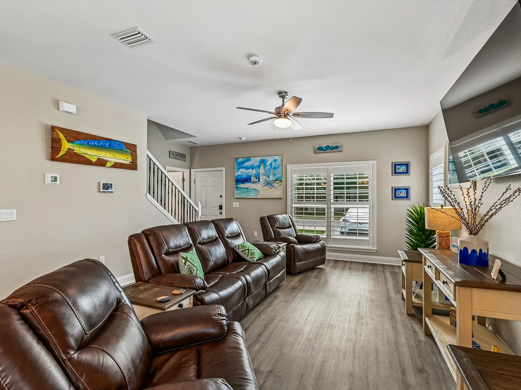 A living room with leather seating, a ceiling fan, and windows with blinds.
