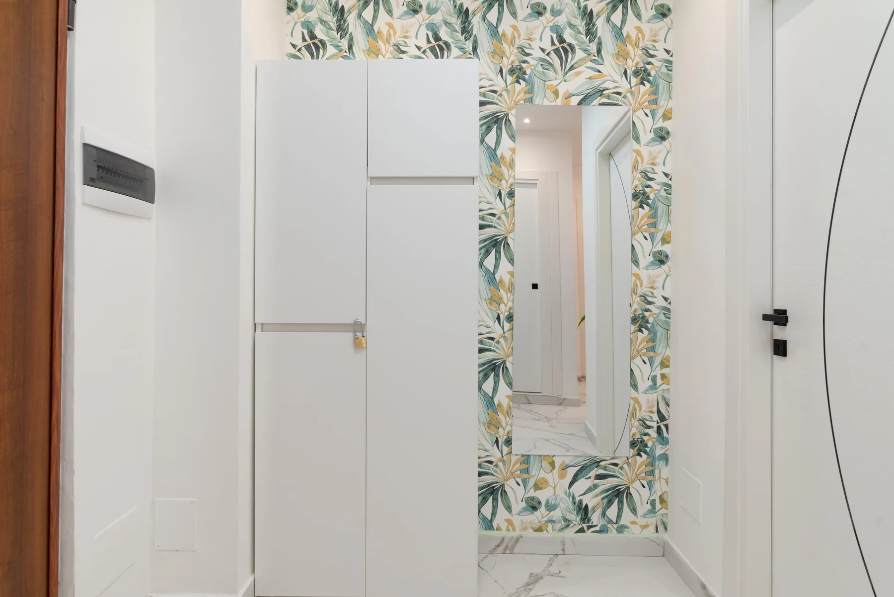 A bright hallway with a full-length mirror framed by leafy wallpaper.