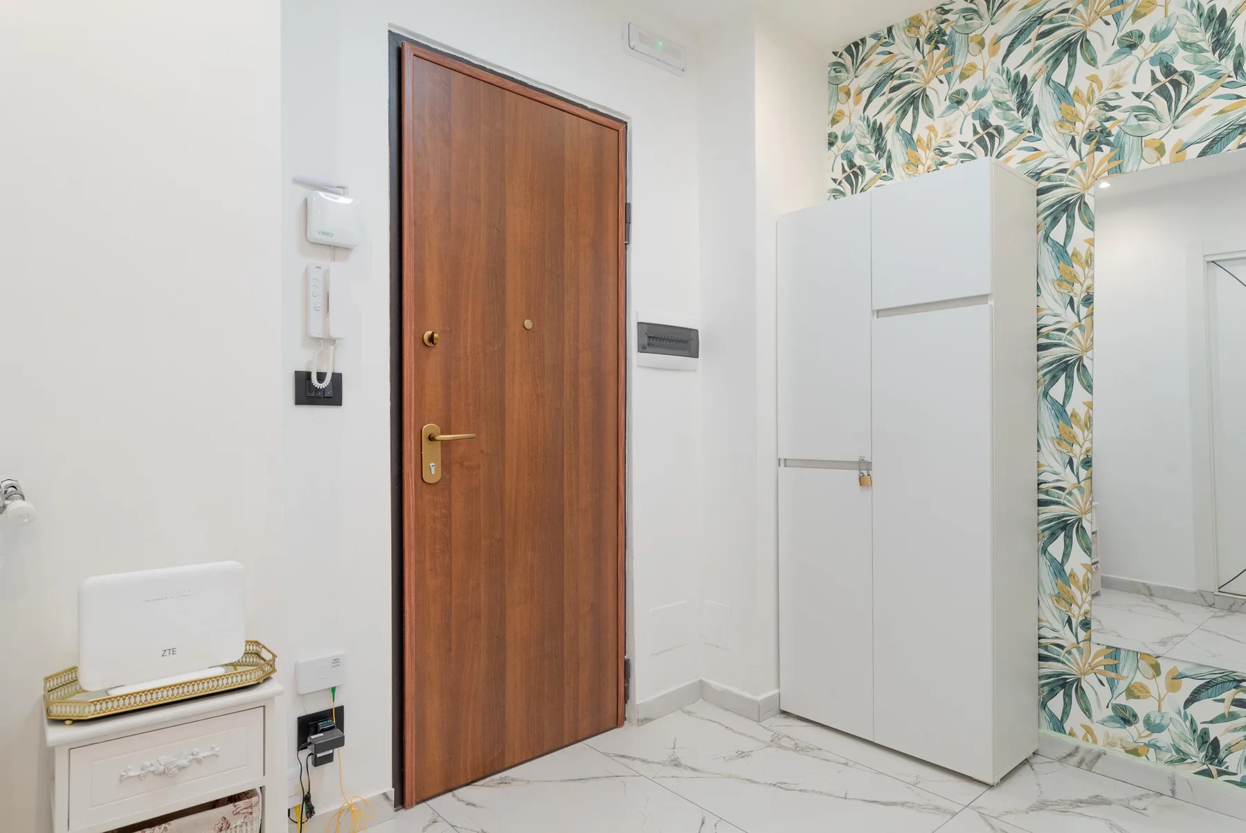 An apartment entryway with a wooden door and a tall white cabinet.