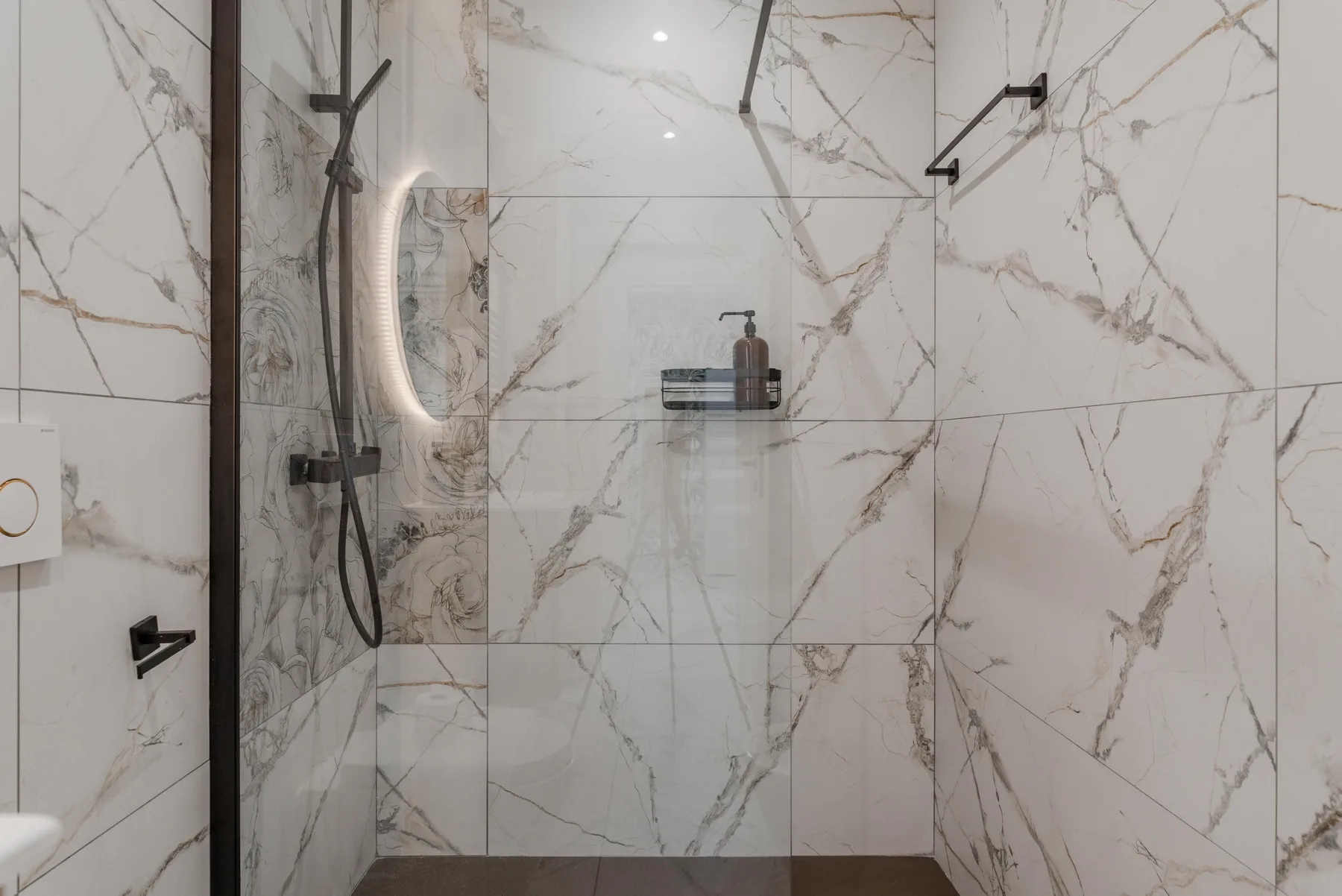 A tiled shower area with a wall-mounted showerhead and shelf.