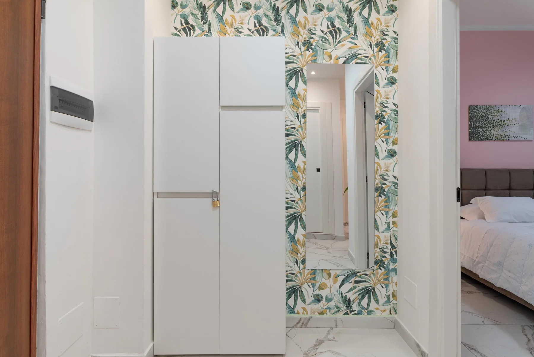 A hallway with a tall white cabinet and a leafy patterned wall around the mirror.