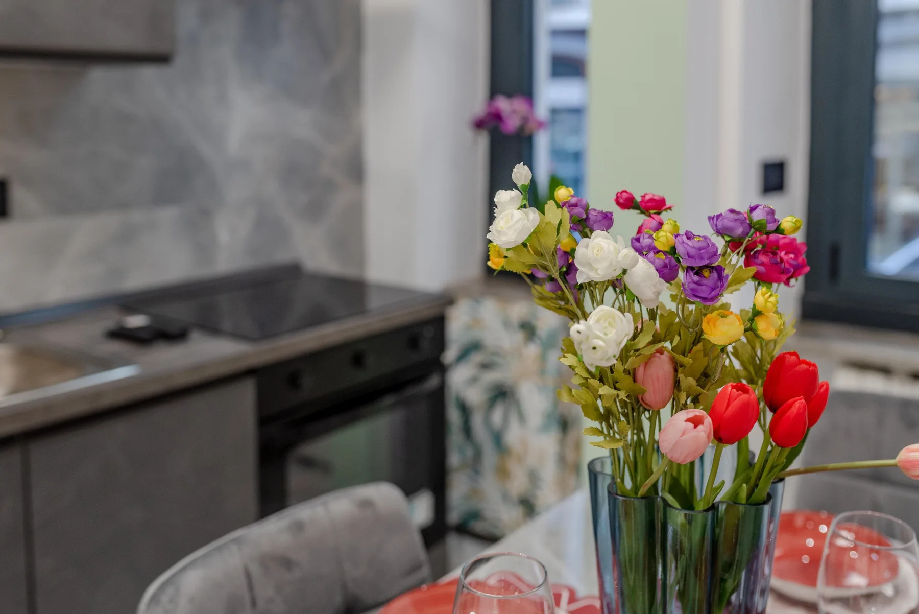 A dining table with a colorful bouquet of flowers beside a kitchen.
