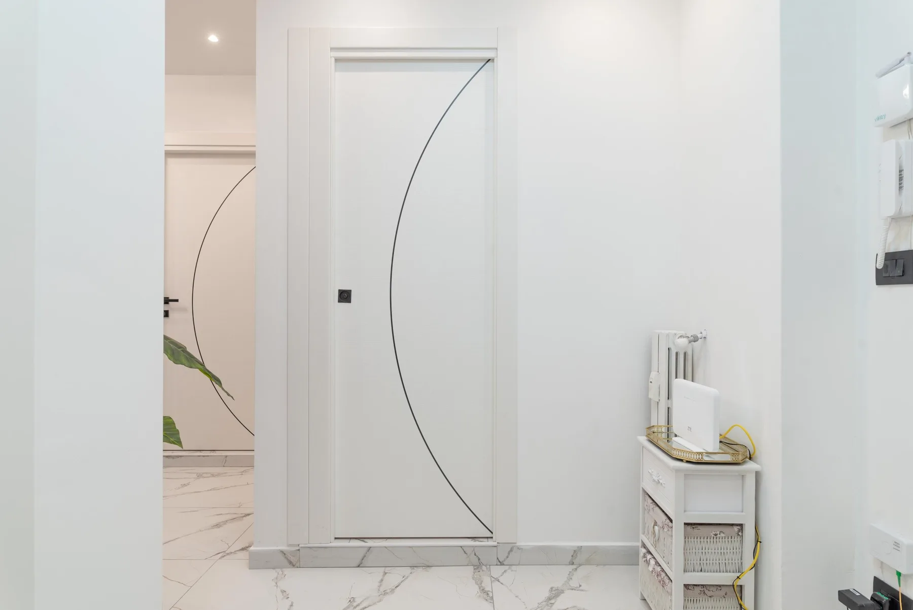 A bright white hallway with a closed door and a small storage cart.