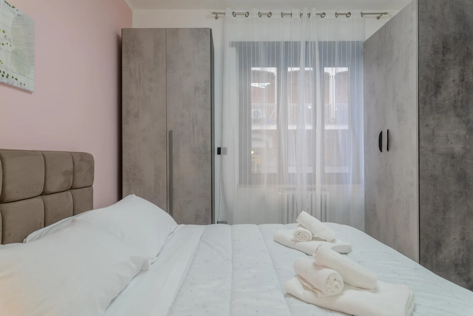 A bedroom with a bed, wardrobes, and a window with sheer curtains.