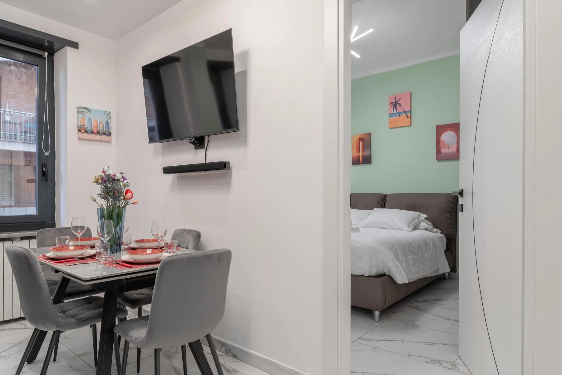 Dining area with a set table beside a bedroom with a mint-green wall.