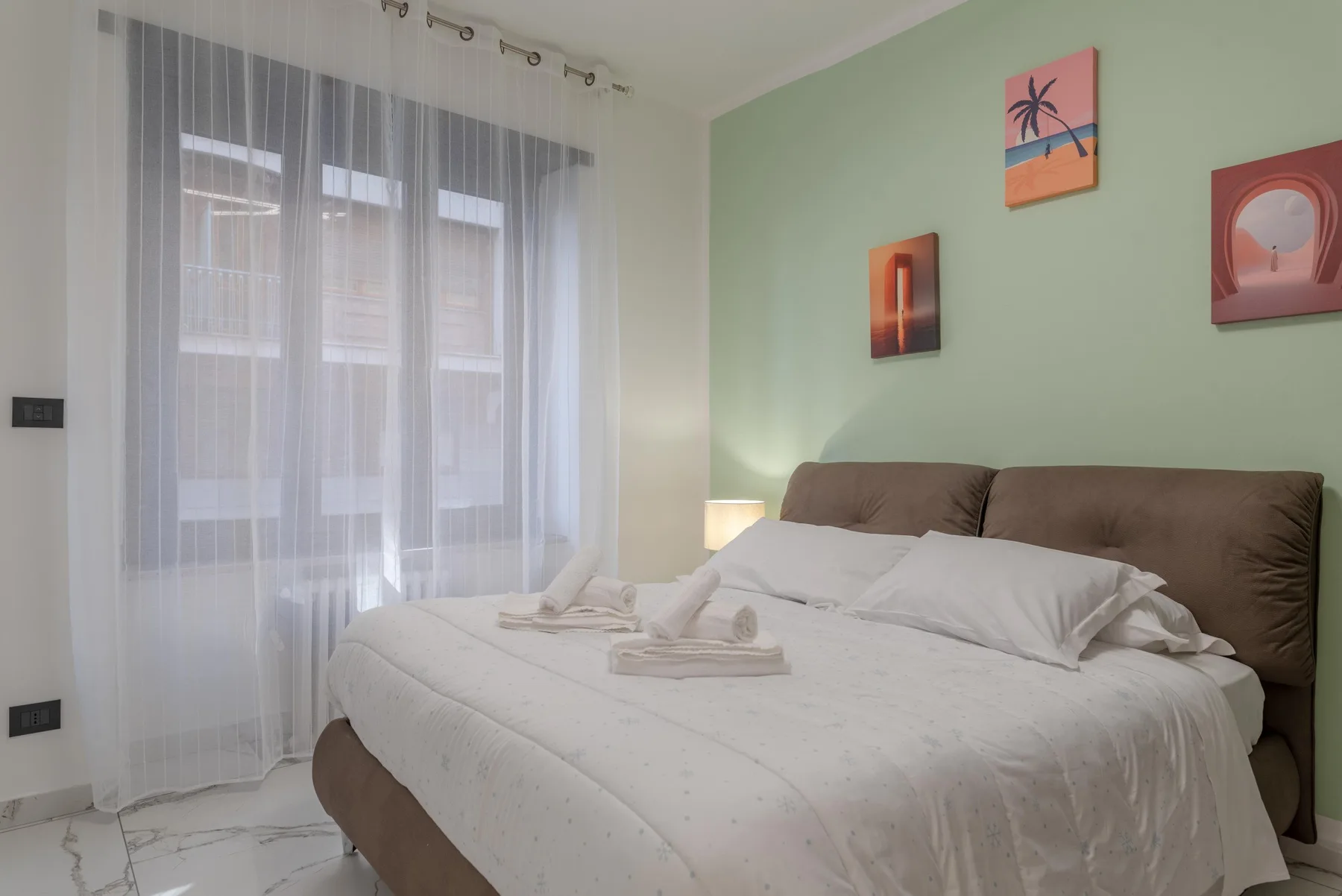 A bedroom with a large bed beneath three colorful wall prints.