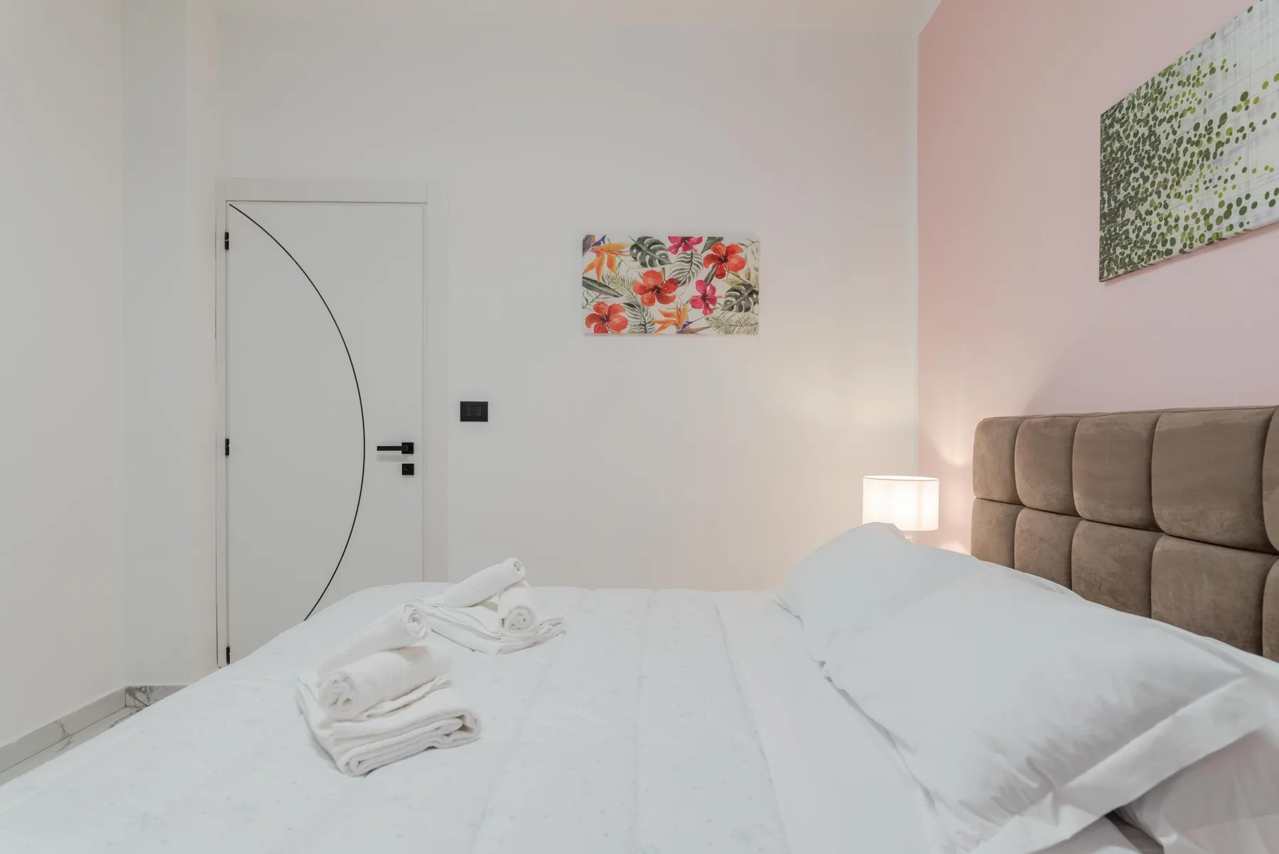 A bedroom with a neatly made bed and colorful floral wall art.