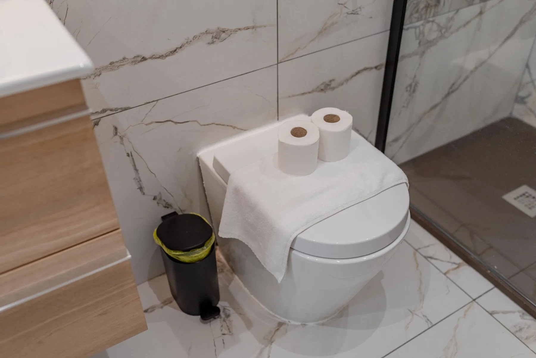A tiled bathroom with a toilet and a small waste bin beside the vanity.