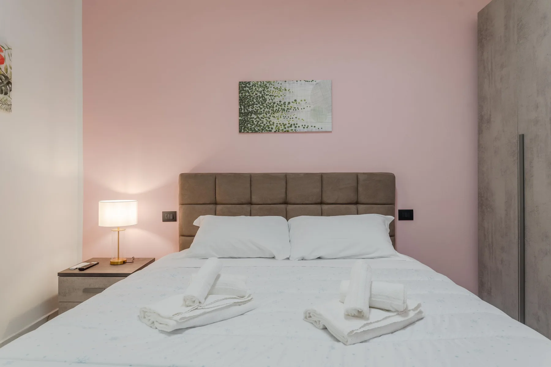 A bedroom with a neatly made bed against a pink wall.