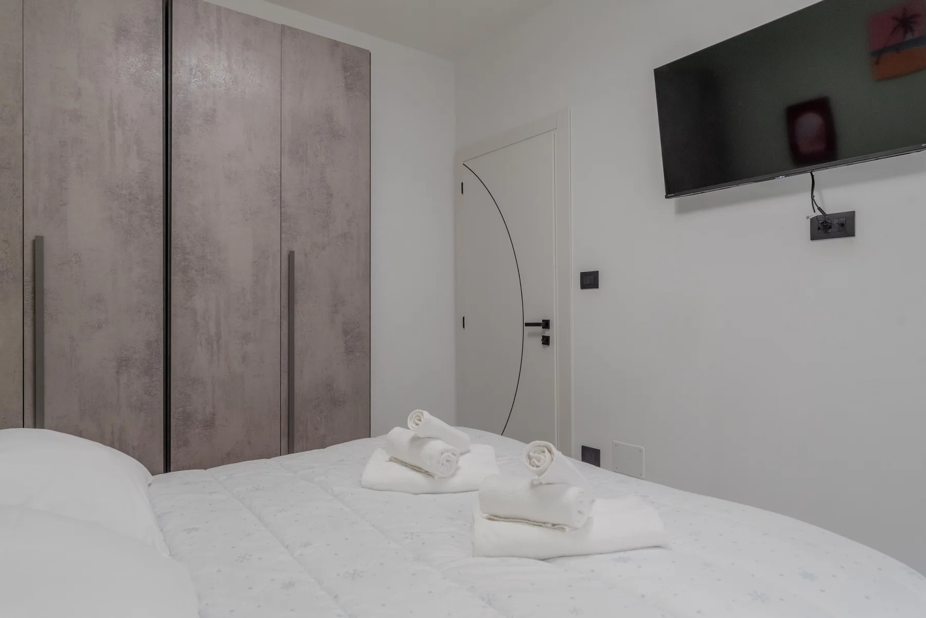 A bedroom with a bed and folded towels beneath a wall-mounted television.