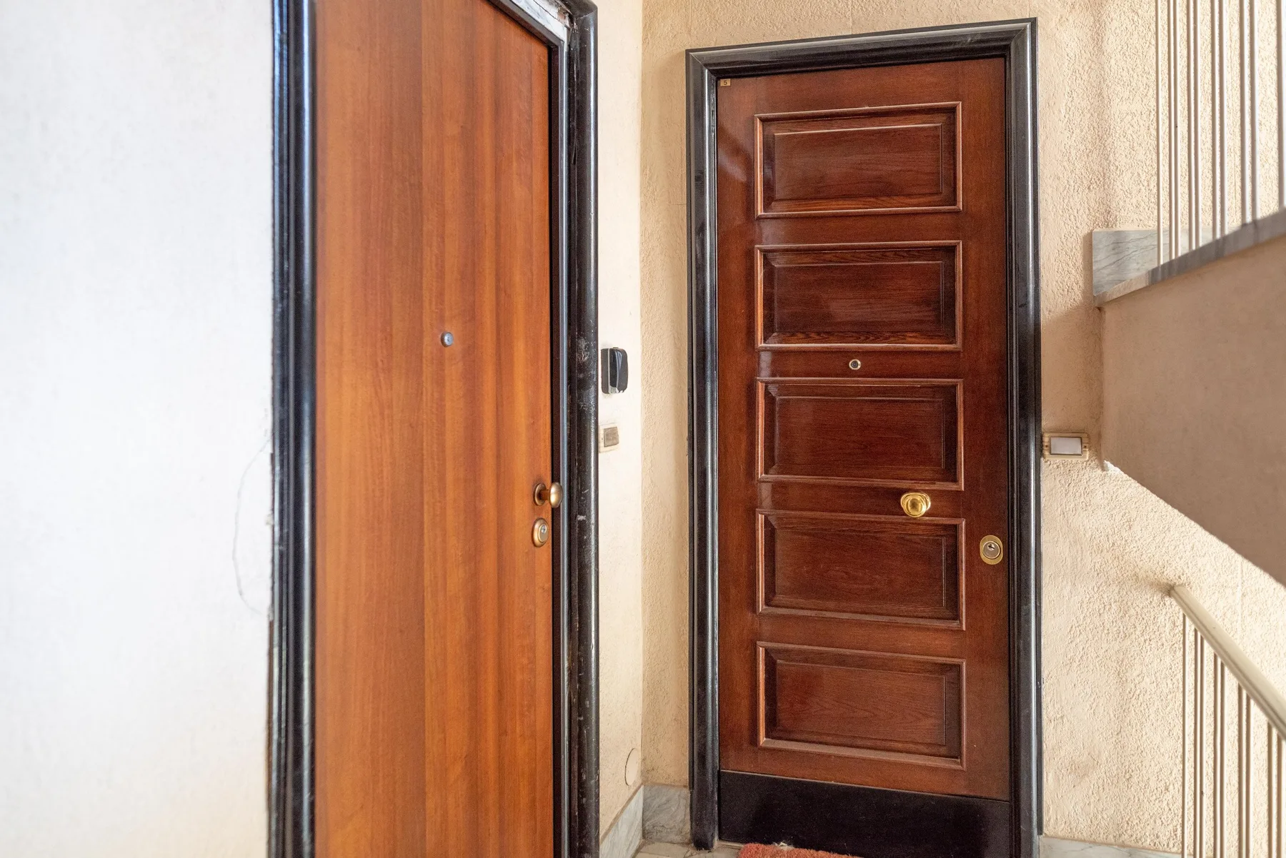 An entryway with two wooden doors and a staircase railing.