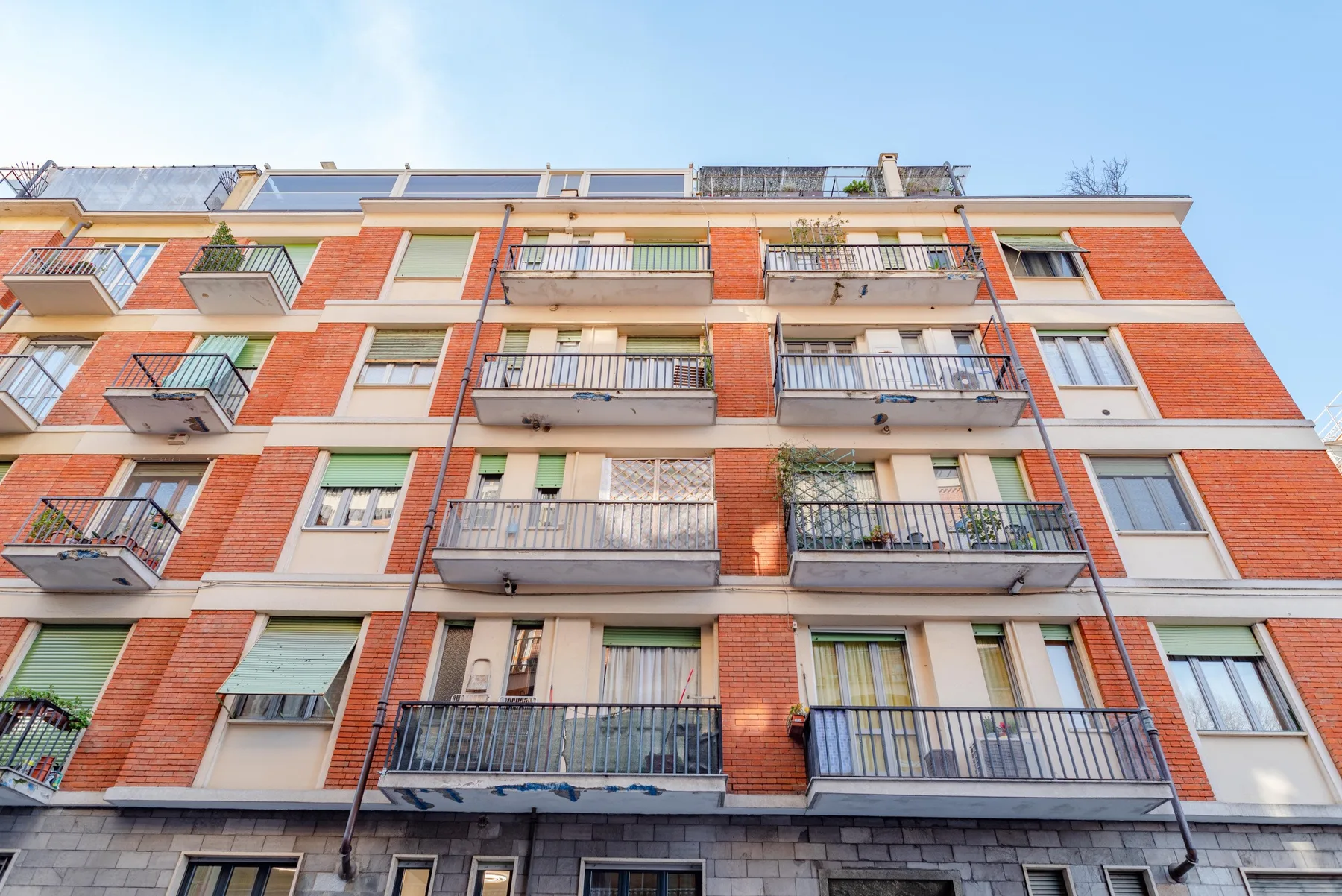 A red-brick apartment building with balconies beneath a clear sky.
