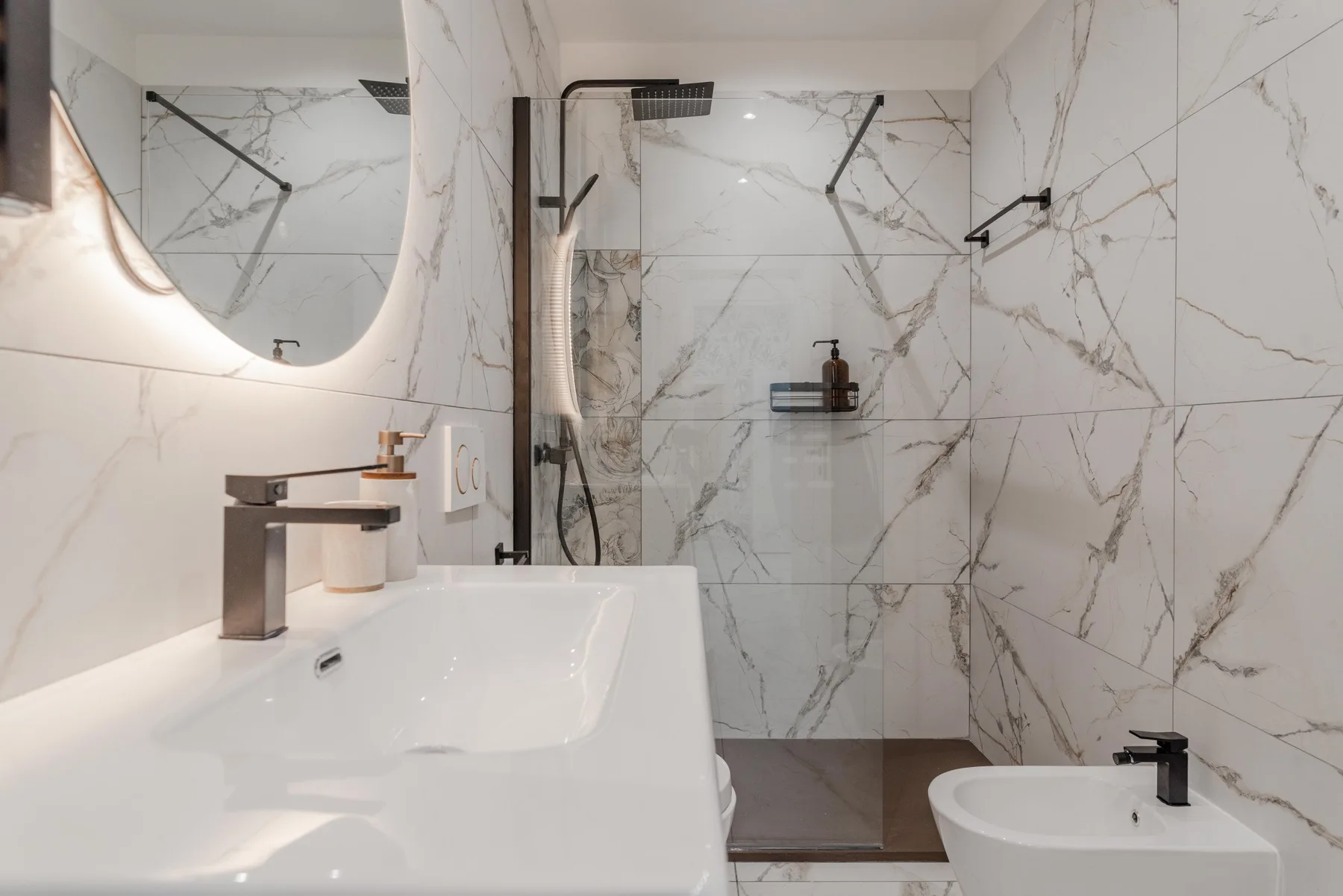 A marble-tiled bathroom with a sink, shower, and bidet.