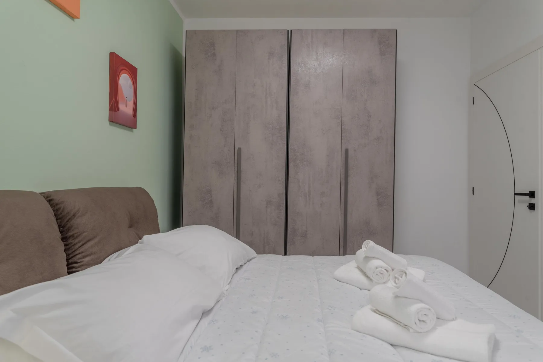 A bedroom with a bed, folded towels, and a tall wardrobe.