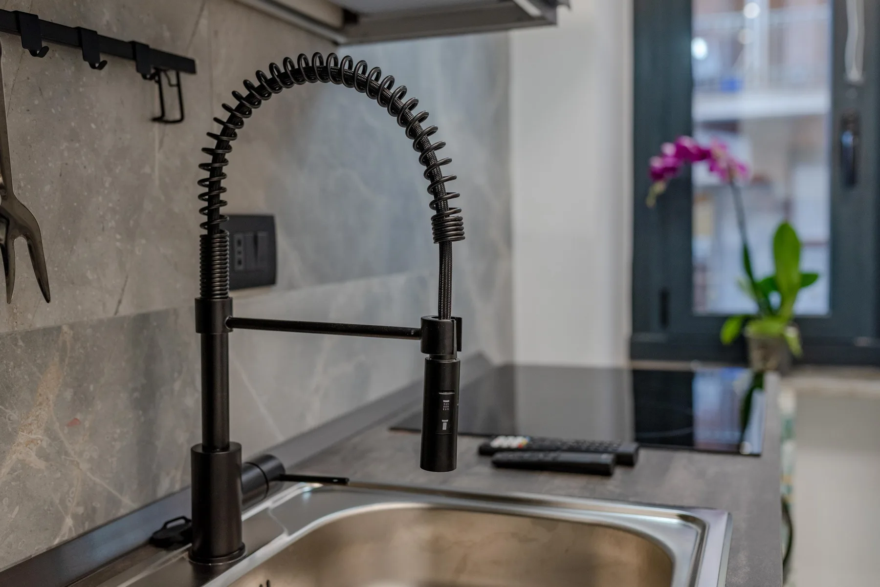 A kitchen sink with a tall spring-coil faucet sits beneath a window.