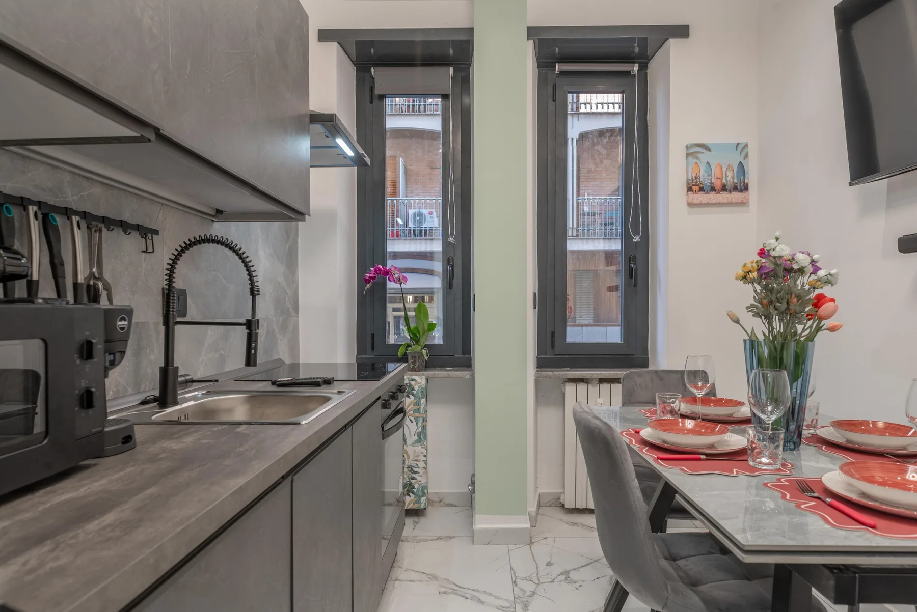A compact kitchen and dining area with a table set beside tall windows.