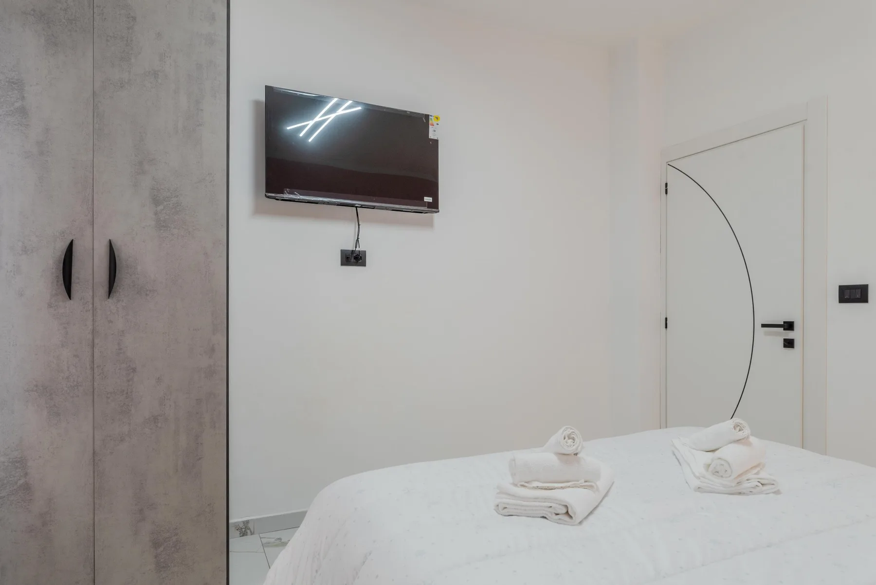 A bedroom with a bed, wall-mounted television, and wardrobe.